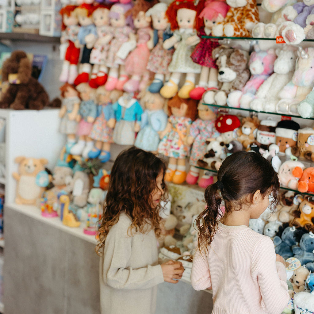 Two children standing in front of a wall filled with various teddy bears, dolls, Jellycats and Palm Pals.